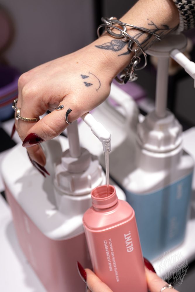 A tattooed hand reaching for hair-colour bottles