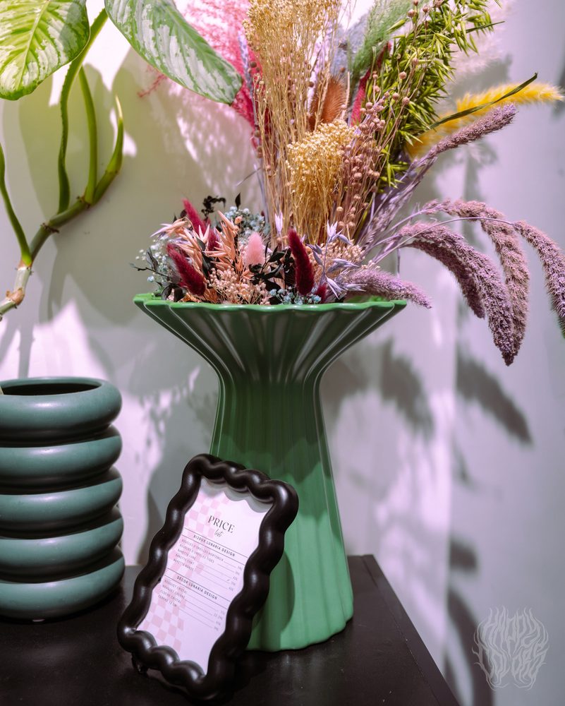 A green vase of dried flowers beside a wavy mirror
